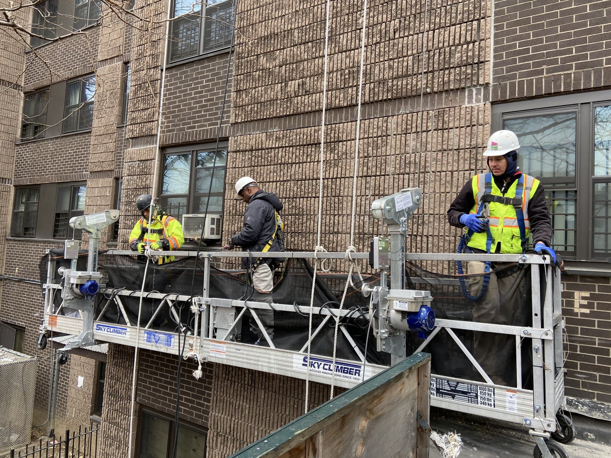 Licensed structural engineers on a swing stage performing a commercial facade assessment in Queens, New York